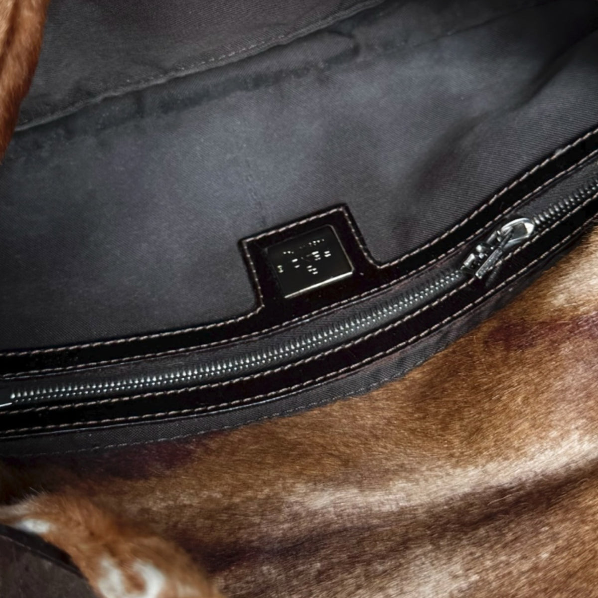 Interior of a Fivedotsvintage FENDI vintage shoulder bag featuring dark brown fabric lining and a metal logo plaque.